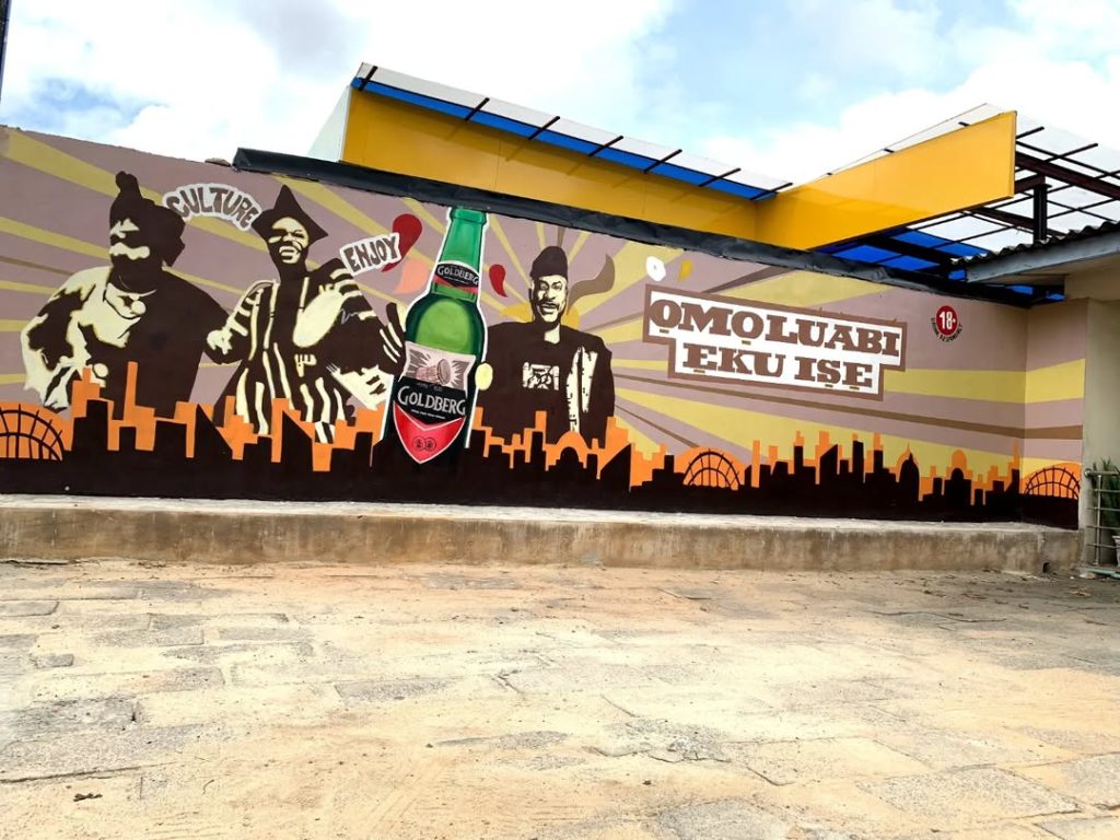 Colorful mural art in Lagos featuring cultural figures, city skyline, and a Goldberg beer design with the text “Omoluabi Eku Ise,” showcasing creativity and modern mural artists in Lagos.